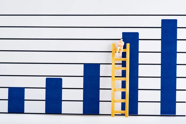 Figura de las personas de plástico en la escalera en la superficie blanca con gráficos analíticos azules en el fondo, concepto de igualdad - foto de stock