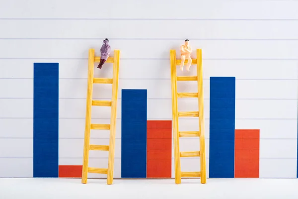 Figuras de la gente en escaleras en la superficie blanca cerca de gráficos azules y rojos en el fondo, concepto de igualdad - foto de stock