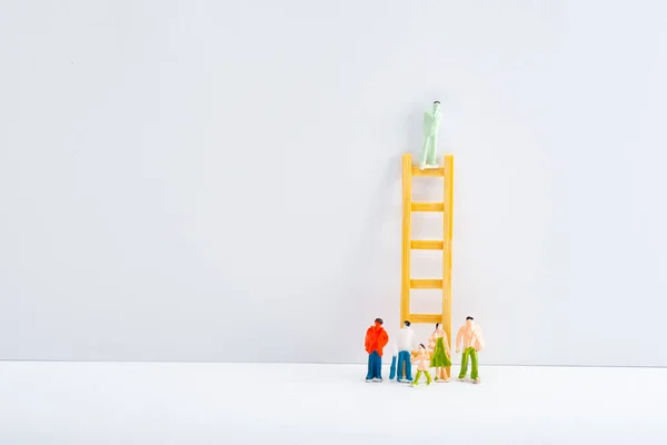 People figures near ladder with toy on white surface on grey background, concept of equality rights — Stock Photo