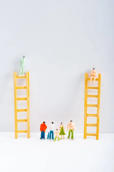 Figuras de plástico cerca de muñecas en escaleras sobre superficie blanca sobre fondo gris, concepto de derechos de igualdad - foto de stock