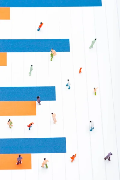 Top view of plastic people figures on surface with blue and orange charts, concept of equality — Stock Photo