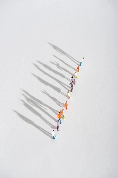 Вид сверху ряда пластиковых фигур людей с тенью на белой поверхности — стоковое фото