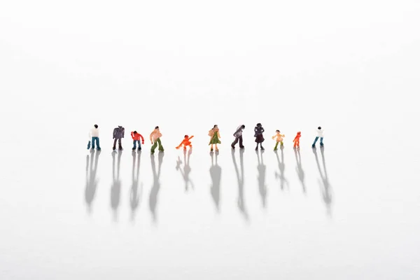 High angle view of row of plastic people figures with shadow on white surface — Stock Photo