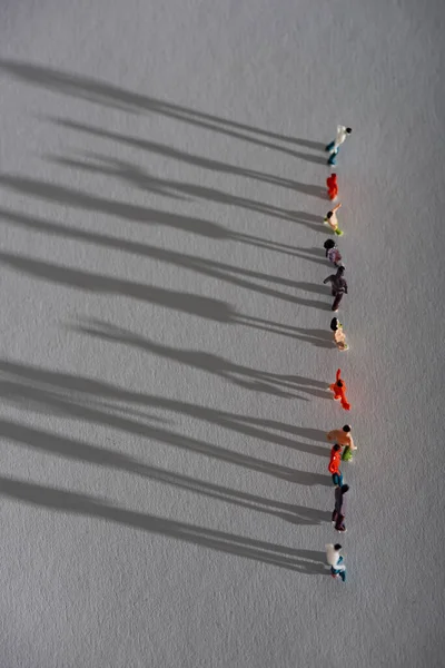 Vista superior de fila de figuras de personas de plástico con sombra en superficie gris - foto de stock