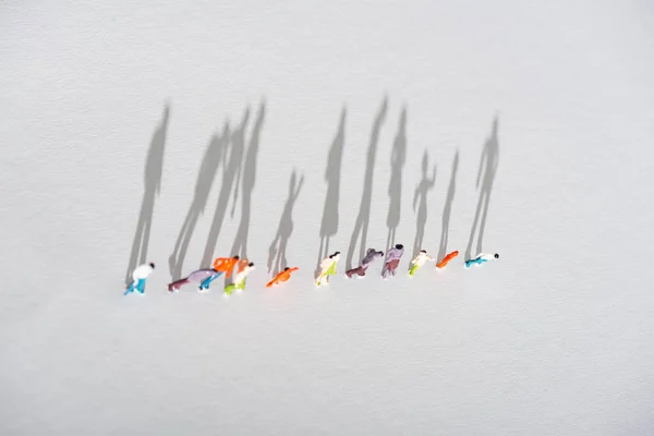 Visão superior da linha de figuras de pessoas de plástico na superfície branca com sombra — Fotografia de Stock