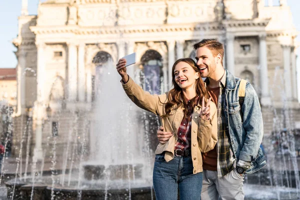 Casal feliz tomando selfie perto da fonte na cidade — Fotografia de Stock