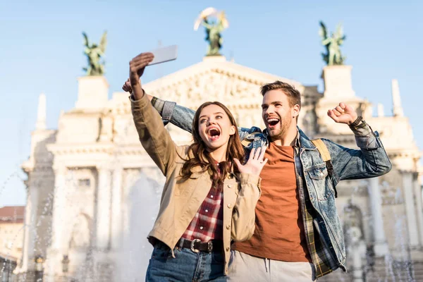 Casal animado tomando selfie perto de fonte na cidade — Fotografia de Stock