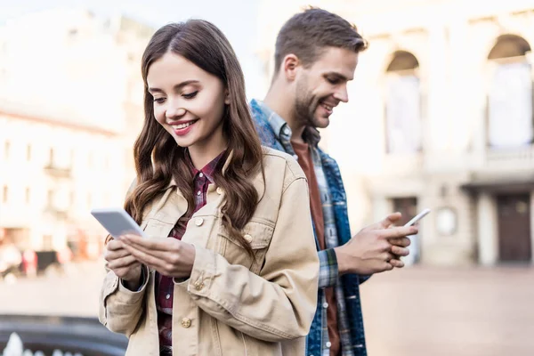 Жінка і чоловік посміхаються і спілкуються зі смартфонами — стокове фото