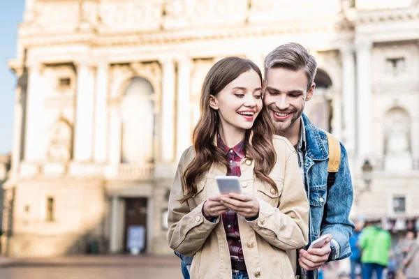 Selective focus of boyfriend and girlfriend smiling with smartphones in city — Stock Photo