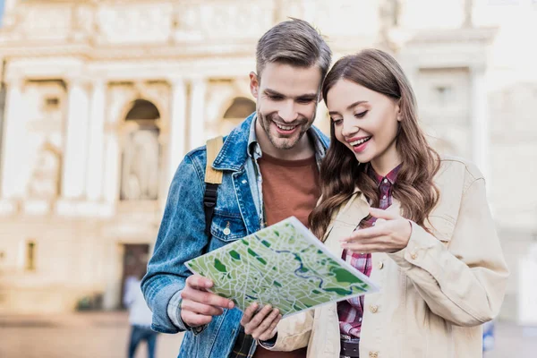 Selective focus of couple looking at map and smiling in city — Stock Photo