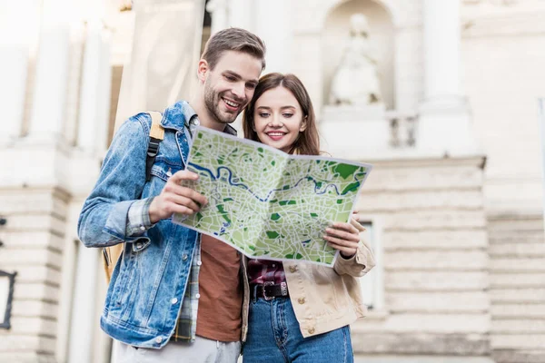 Pareja mirando el mapa juntos y sonriendo en la ciudad - foto de stock