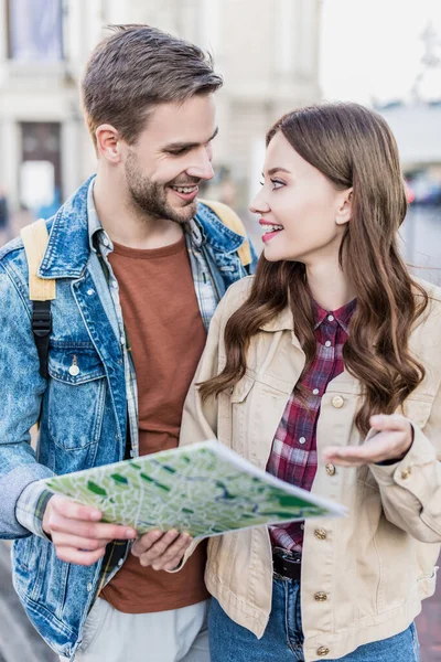 Foco seletivo de namorado e namorada olhando um para o outro, sorrindo e segurando mapa — Fotografia de Stock