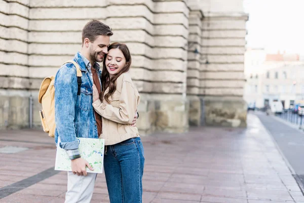 Selective focus of happy couple hugging and smiling with map in city — Stock Photo