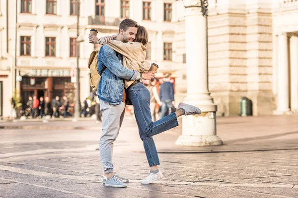 Boyfriend and girlfriend holding disposable cups of coffee and hugging in city — Stock Photo