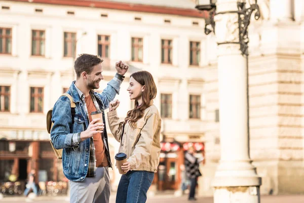 Aufgeregter Freund und Freundin mit Einwegbechern Kaffee, die einander anschauen und in der Stadt lächeln — Stockfoto