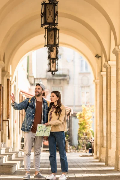 Foco seletivo de namorado apontando com a mão e namorada com mapa animado e surpreso na cidade — Fotografia de Stock