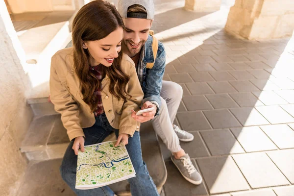 Focus selettivo della coppia seduta sulle scale con mappa e utilizzando lo smartphone in città — Foto stock