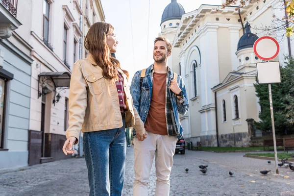 Selective focus of couple looking at each other and holding hands in city — Stock Photo