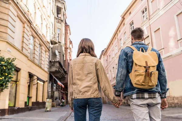 Vista trasera de pareja cogida de la mano con mochila en la ciudad - foto de stock