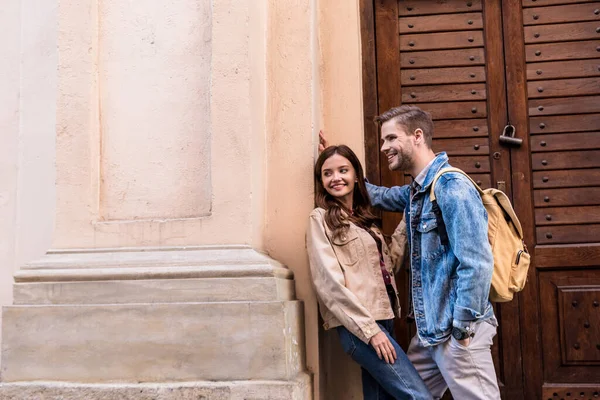 Novio y novia sonriendo cerca de la pared en la ciudad - foto de stock