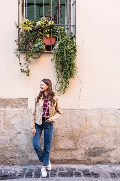 Vue pleine longueur de la fille avec la main dans la poche regardant loin près du mur — Photo de stock