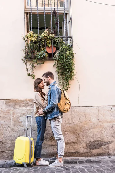 Couple with backpack and suitcase hugging near wall in city — Stock Photo