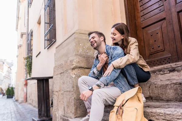 Selective focus of girlfriend hugging boyfriend and smiling on stairs in city — Stock Photo