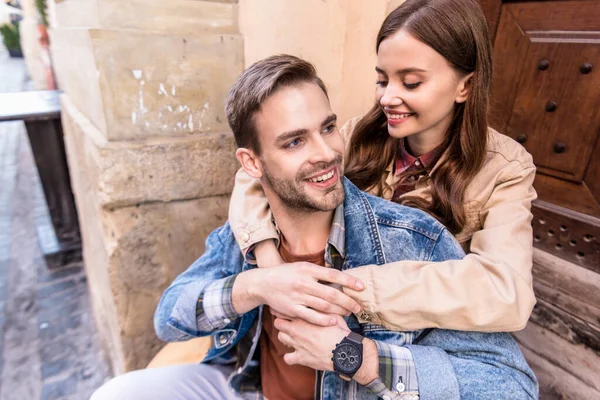 Enfoque selectivo de novia abrazando novio y sonriendo cerca de la ciudad - foto de stock