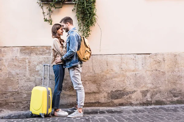 Пара з рюкзаком і валіза обіймається біля стіни в місті — стокове фото