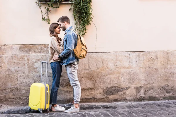 Coppia con zaino e valigia che si abbraccia vicino al muro in città — Foto stock