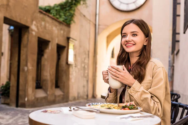 Вибірковий фокус жінки, яка посміхається і тримає білу чашку чаю в кафе в місті — стокове фото