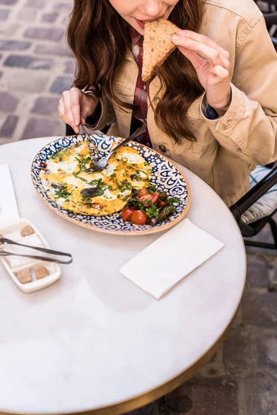 Cropped view of woman eating omelette with bread and salad in cafe in city — Stock Photo