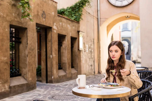 Enfoque selectivo de la mujer comiendo con taza blanca de té en la cafetería de la ciudad - foto de stock