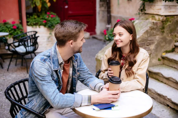 Selective focus of couple with disposable cups of coffee and passports looking at each other in cafe in city — Stock Photo