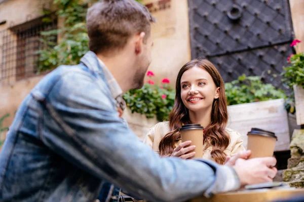 Selective focus of couple with disposable cups of coffee looking at each other in cafe in city — Stock Photo