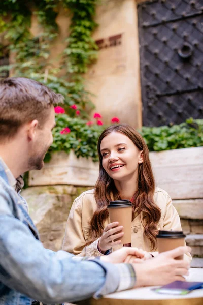 Selective focus of couple with paper cups of coffee looking at each other in cafe in city — Stock Photo