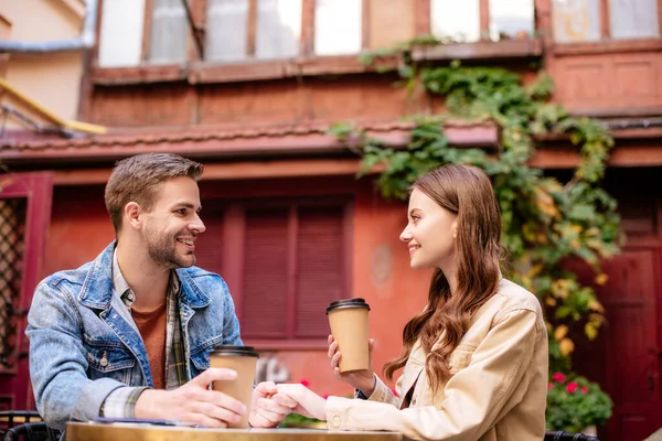 Селективный фокус пары с бумажными чашками кофе, смотрящих друг на друга и улыбающихся в кафе во Львове — стоковое фото