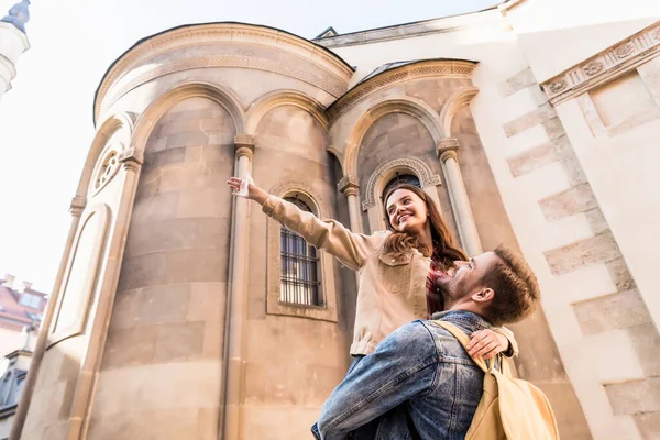 Low angle view of boyfriend holding girlfriend with outstretched hand near building in city — Stock Photo