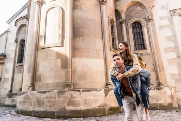 Excited man piggybacking girlfriend near building in city — Stock Photo