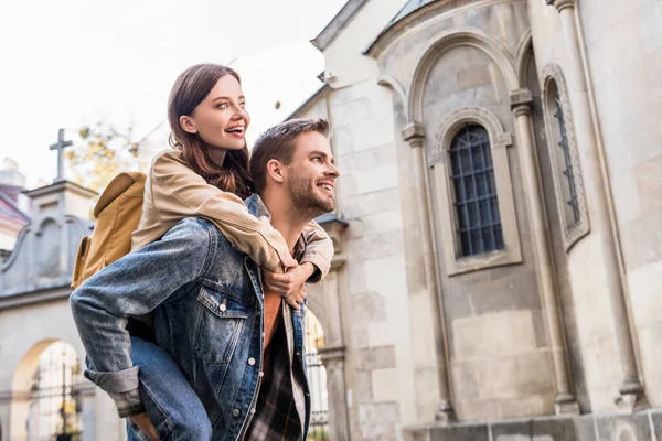 Selective focus of man piggybacking girlfriend near building in city — Stock Photo