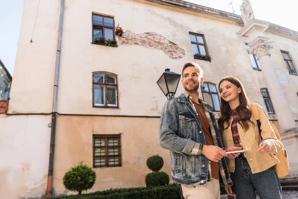 Low angle view of couple with digital tablet looking away and smiling in city — Stock Photo