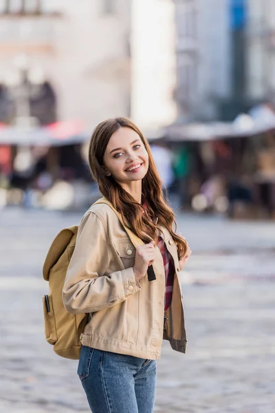 Schöne Frau blickt in die Kamera und lächelt mit Rucksack in der Stadt — Stockfoto