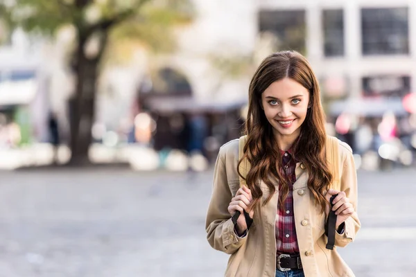 Schöne Mädchen blickt in die Kamera und lächelt mit Rucksack in der Stadt — Stockfoto