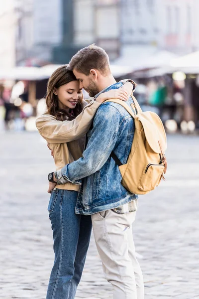 Hombre con mochila abrazándose con hermosa novia en la ciudad - foto de stock