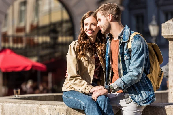 Feliz novia y novio sentados juntos y sonriendo en la ciudad - foto de stock