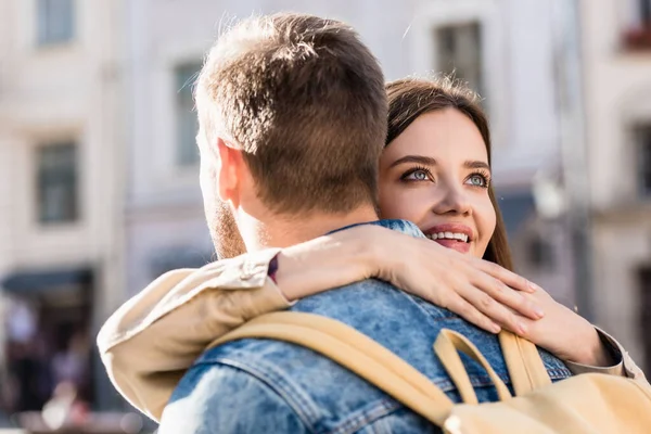 Novia abrazando novio, mirando hacia arriba y sonriendo en la ciudad - foto de stock