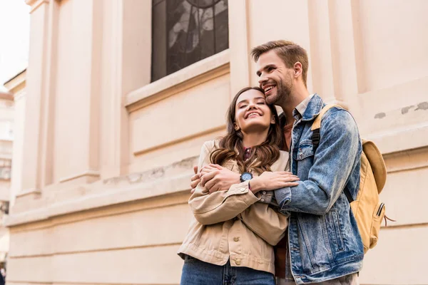 Hombre y mujer con los ojos cerrados abrazando y sonriendo en la ciudad - foto de stock