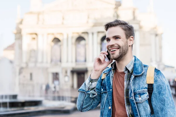Hombre guapo sonriendo y hablando en el teléfono inteligente en la ciudad - foto de stock