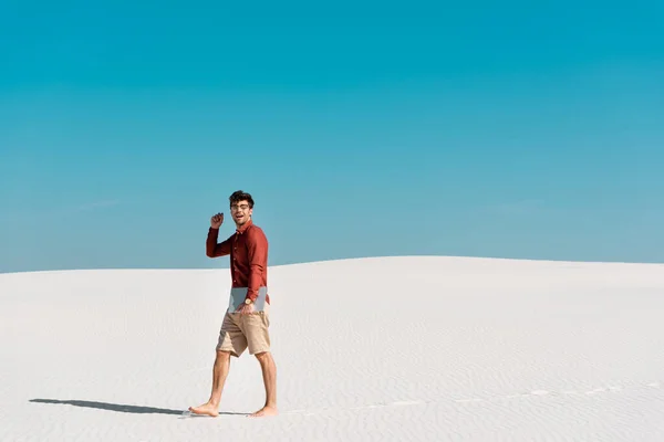 Beau pigiste sur la plage de sable avec ordinateur portable contre ciel bleu clair — Photo de stock