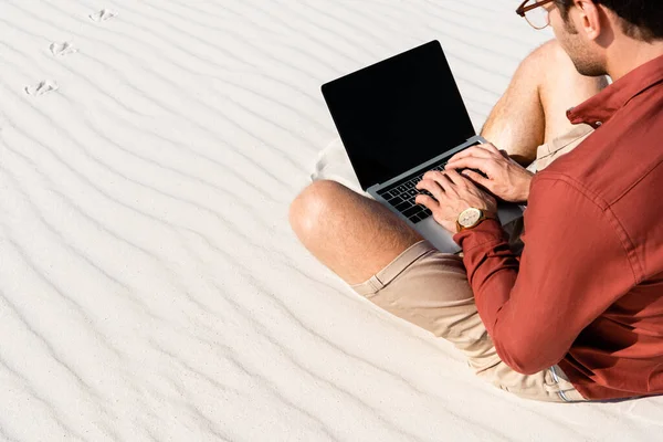 Freelancer sitting on sandy beach with laptop against clear blue sky — Stock Photo